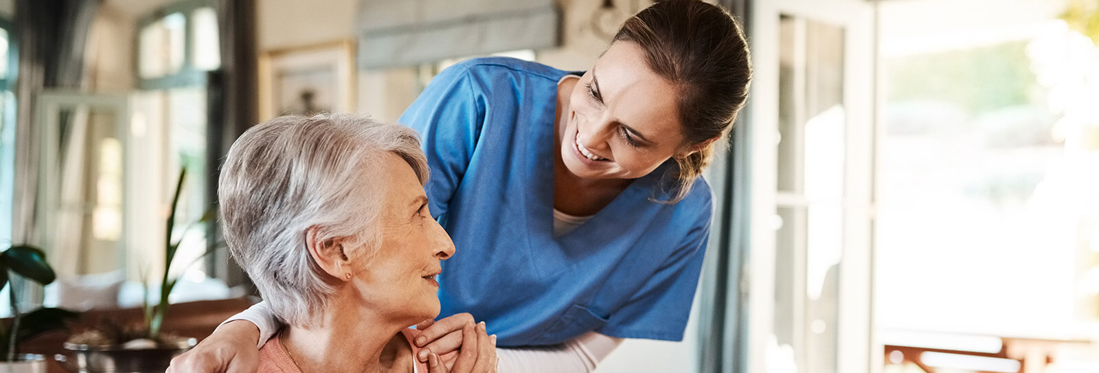 A nurse stands behind a patient, comforting them with a warm smile